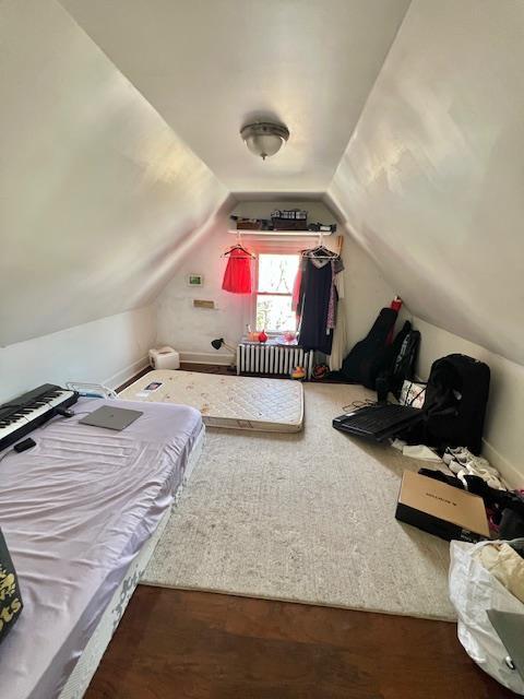 bedroom featuring vaulted ceiling, radiator heating unit, and wood finished floors