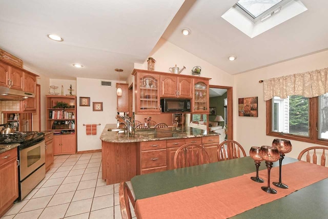 kitchen featuring stainless steel range with gas cooktop, vaulted ceiling with skylight, black microwave, glass insert cabinets, and visible vents
