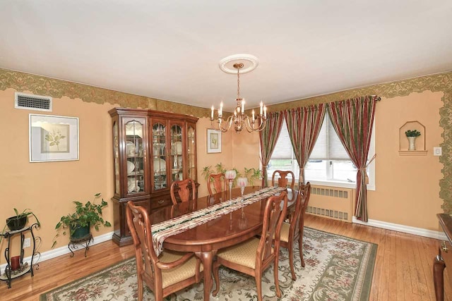 dining area featuring a chandelier, radiator heating unit, visible vents, and wood finished floors