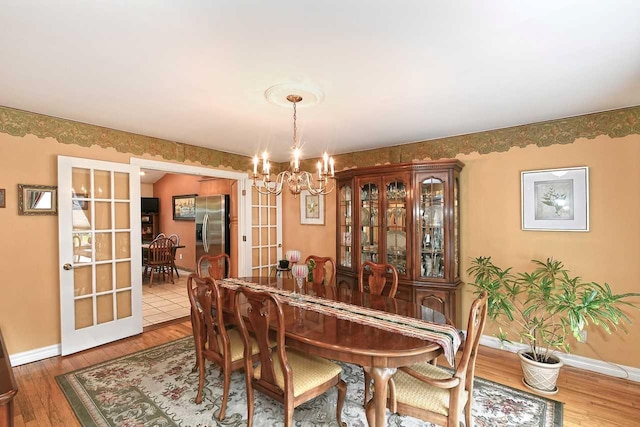 dining room featuring wood finished floors, baseboards, a notable chandelier, and french doors