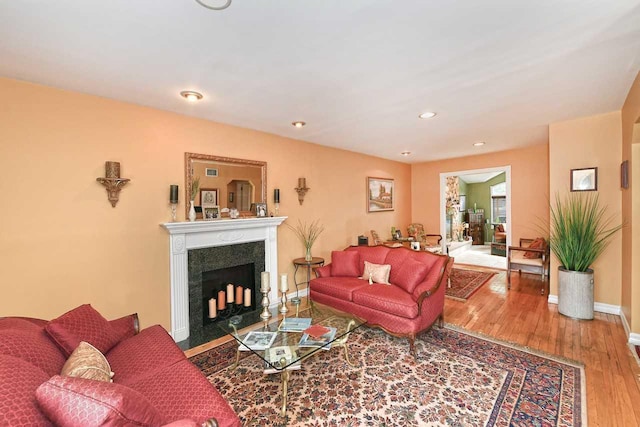 living room featuring a fireplace with flush hearth, baseboards, wood finished floors, and recessed lighting