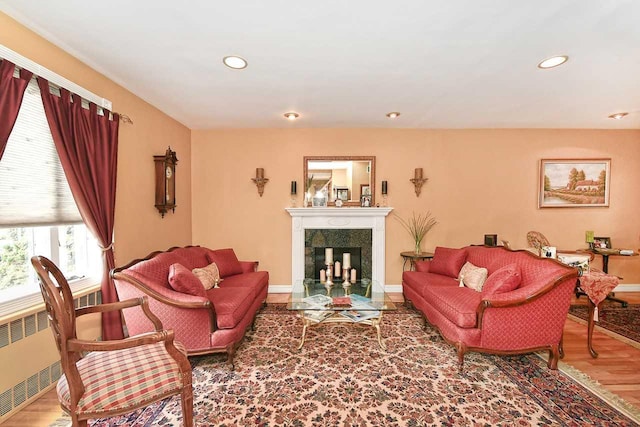 living room featuring wood finished floors, a fireplace with flush hearth, radiator, baseboards, and recessed lighting
