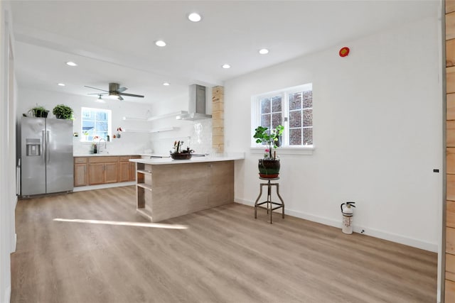 kitchen featuring wall chimney range hood, open shelves, a sink, light wood-type flooring, and stainless steel fridge