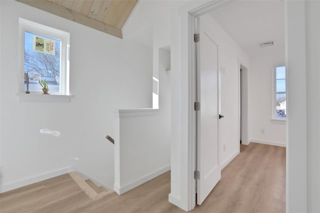 hall featuring light wood-type flooring, baseboards, visible vents, and an upstairs landing