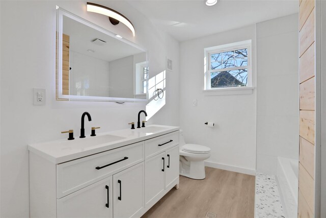 bathroom featuring double vanity, wood finished floors, toilet, and a sink