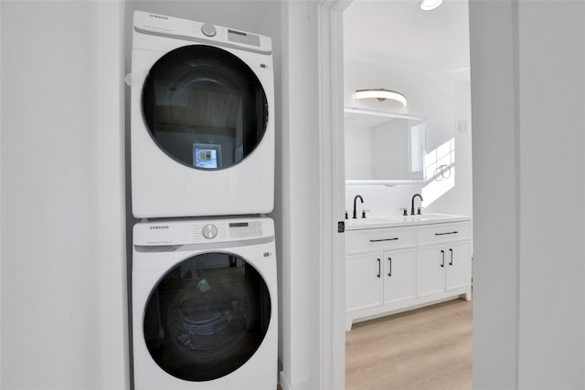 clothes washing area featuring stacked washer / drying machine, laundry area, wet bar, a sink, and light wood-style floors