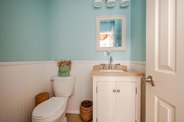 half bathroom featuring a wainscoted wall, toilet, and vanity