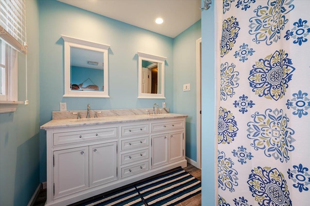bathroom featuring double vanity, tiled shower, and baseboards