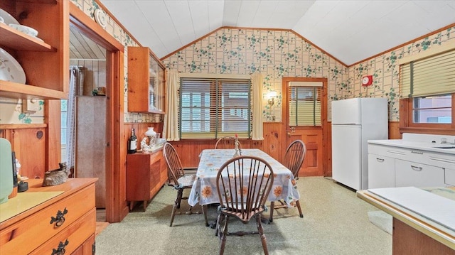 dining space featuring wood walls, wallpapered walls, light floors, a wainscoted wall, and lofted ceiling