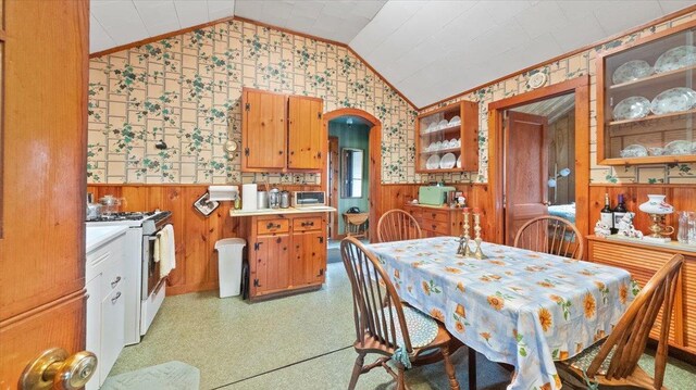 dining space with wainscoting, arched walkways, lofted ceiling, and wallpapered walls