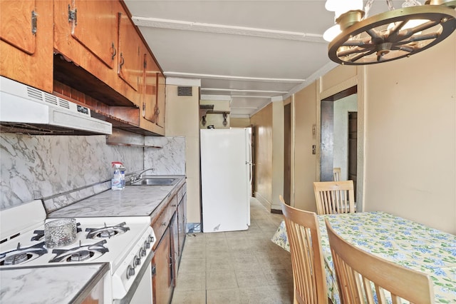 kitchen featuring white appliances, light countertops, under cabinet range hood, a chandelier, and brown cabinets