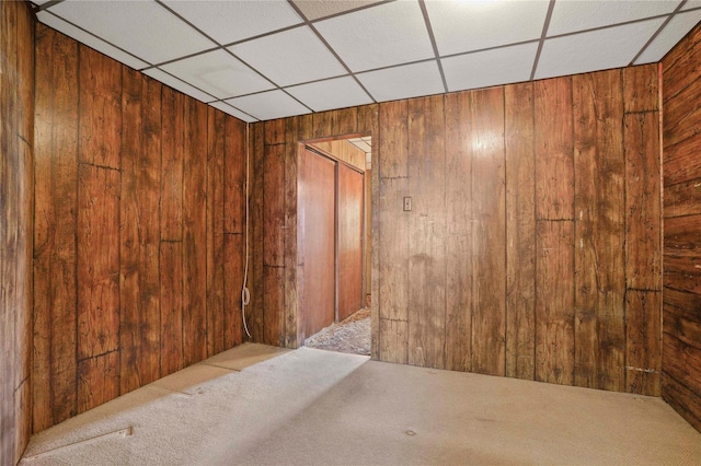 carpeted empty room with wooden walls and a paneled ceiling