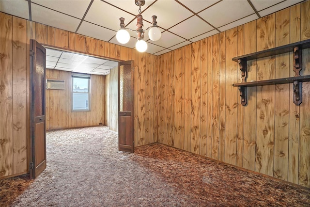 carpeted spare room with wooden walls, a paneled ceiling, a wall mounted air conditioner, and a chandelier