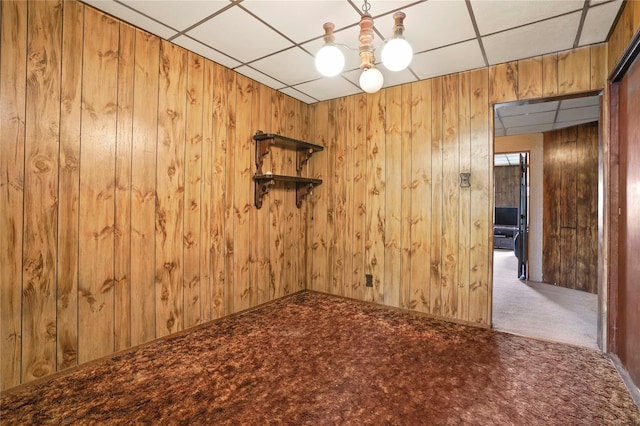 carpeted spare room with a paneled ceiling, a notable chandelier, and wooden walls