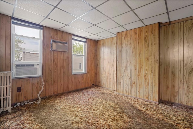 carpeted spare room with a paneled ceiling, a wall mounted AC, wood walls, baseboards, and cooling unit