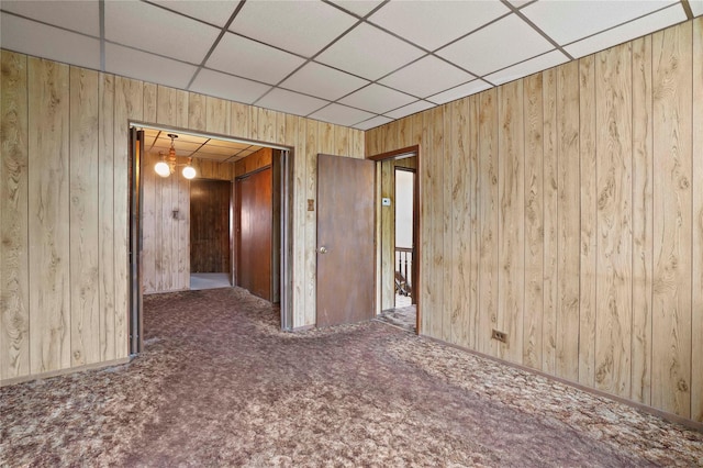 unfurnished room with carpet floors, wood walls, baseboards, and a drop ceiling