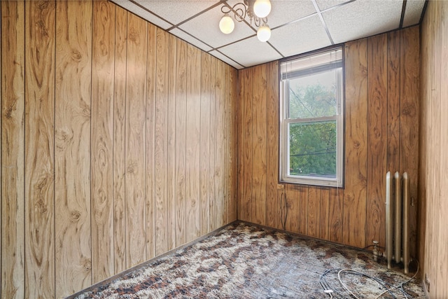 carpeted spare room featuring a drop ceiling, radiator heating unit, and wooden walls