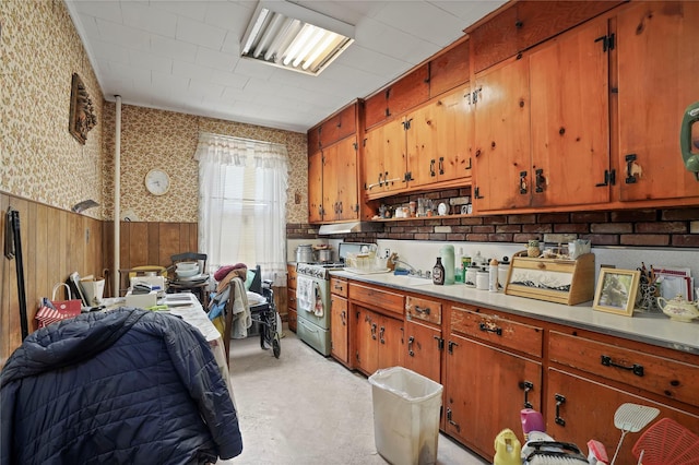 kitchen with stainless steel range with gas cooktop, wallpapered walls, brown cabinetry, and light countertops
