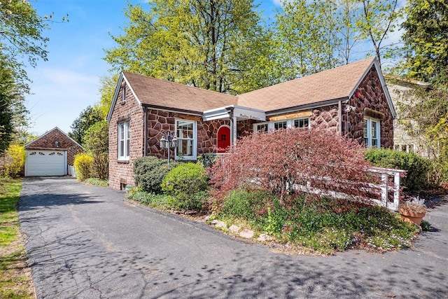 single story home with driveway, an outbuilding, a detached garage, stone siding, and roof with shingles