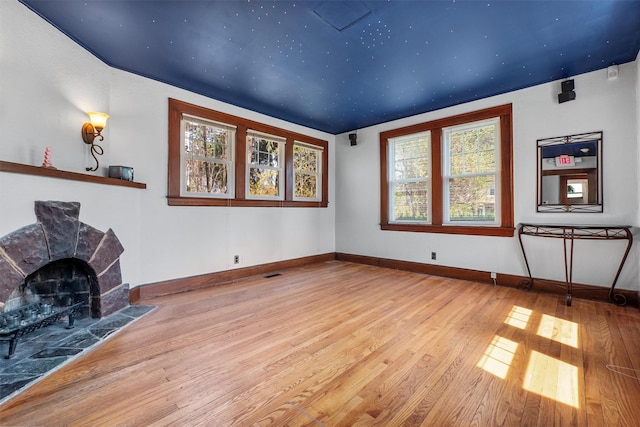 unfurnished living room featuring wood-type flooring, baseboards, visible vents, and a fireplace