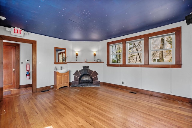 unfurnished room featuring a sink, plenty of natural light, light wood finished floors, baseboards, and visible vents