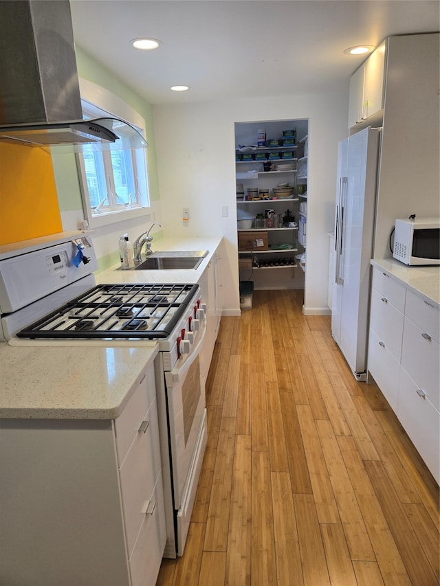 kitchen with ventilation hood, light wood finished floors, a sink, white appliances, and white cabinetry