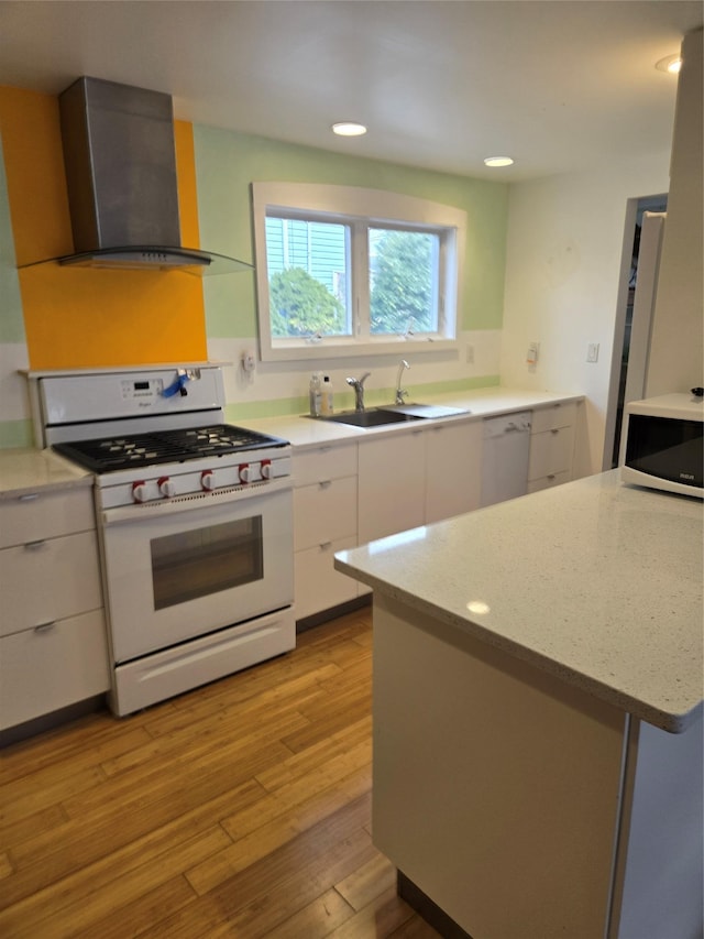 kitchen with wall chimney range hood, a sink, white appliances, modern cabinets, and white cabinets