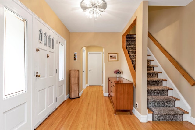 entryway with baseboards, arched walkways, stairs, and light wood-type flooring