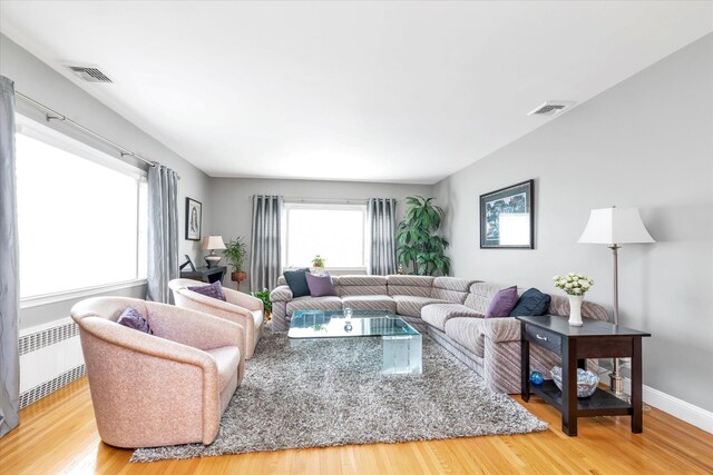living area featuring baseboards, radiator heating unit, light wood finished floors, and visible vents