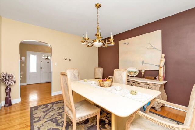 dining space featuring arched walkways, light wood-type flooring, baseboards, and a notable chandelier