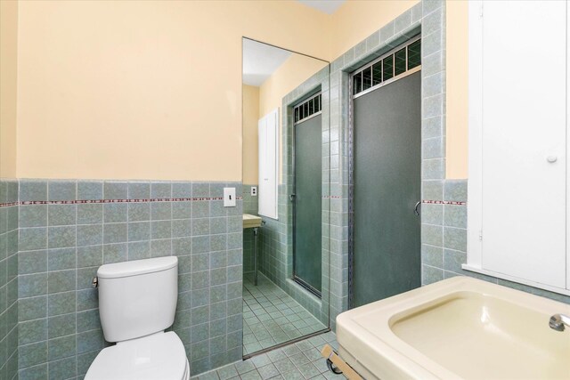 bathroom featuring a wainscoted wall, toilet, tile walls, tile patterned flooring, and a shower stall