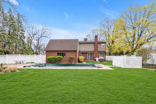 rear view of house with a chimney, a fenced backyard, a yard, a fenced in pool, and brick siding