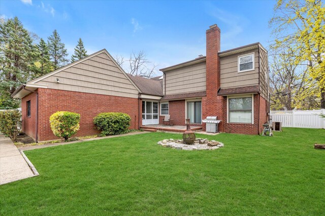 rear view of property with a chimney, fence, a lawn, a fire pit, and brick siding