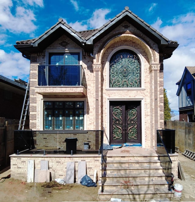 doorway to property featuring brick siding, a tile roof, and fence