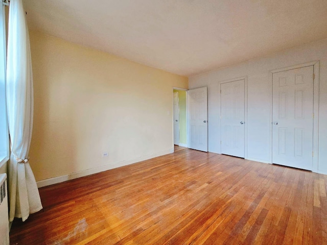 unfurnished bedroom with light wood-style flooring, baseboards, and radiator
