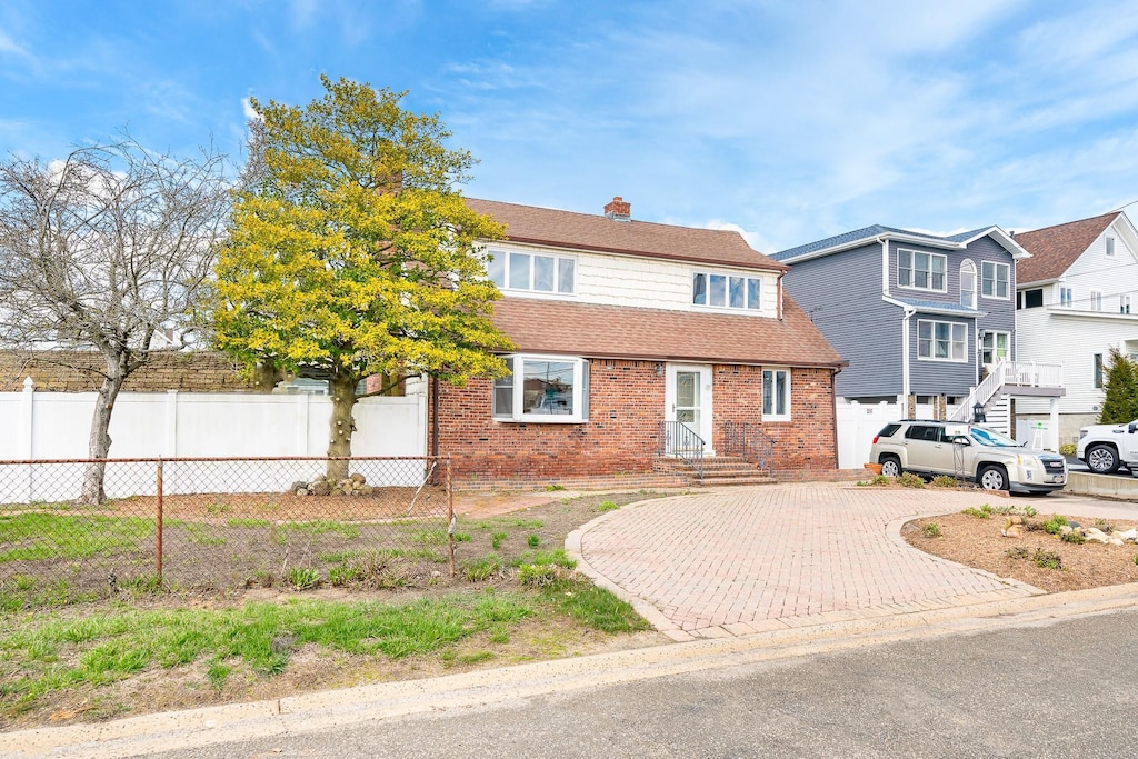 39 Mitchell Ave, Babylon, NY 11702 - view of front facade featuring a chimney, brick siding, decorative driveway, and fence