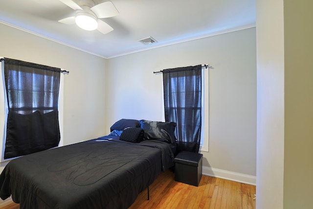 bedroom featuring light wood finished floors, visible vents, ornamental molding, baseboards, and ceiling fan