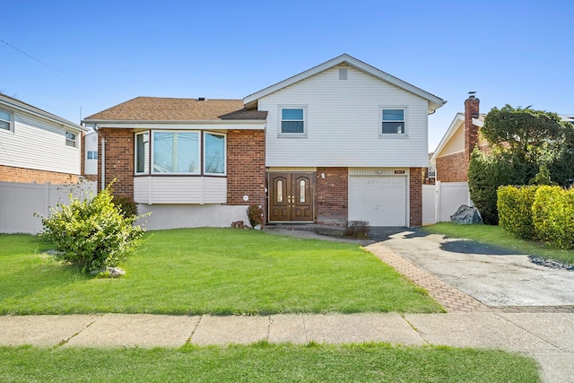split level home with a front lawn, driveway, an attached garage, fence, and brick siding