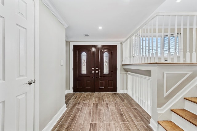 foyer with wood finished floors, visible vents, crown molding, baseboards, and stairs