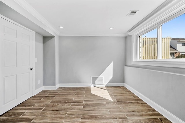 empty room with wood finished floors, visible vents, crown molding, and baseboards