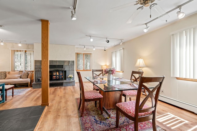 dining room featuring track lighting, a tiled fireplace, ceiling fan, and light wood-type flooring