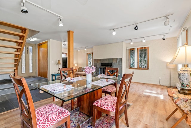 dining space featuring light wood finished floors, track lighting, a tile fireplace, and stairway