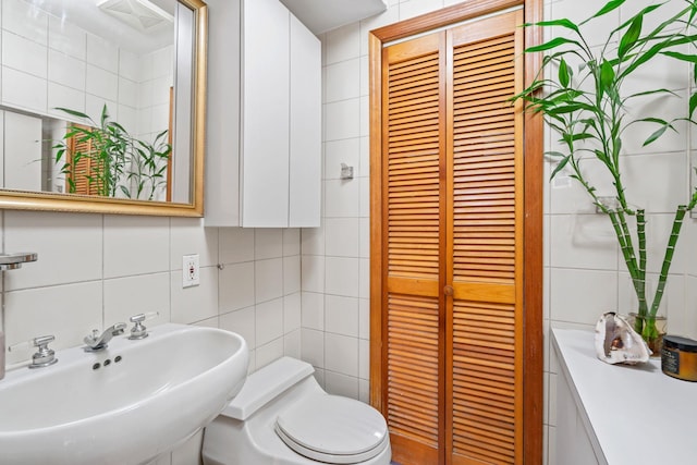 bathroom featuring a sink, toilet, tile walls, decorative backsplash, and a closet