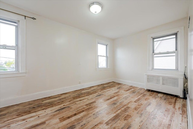 spare room featuring light wood-type flooring, baseboards, and radiator