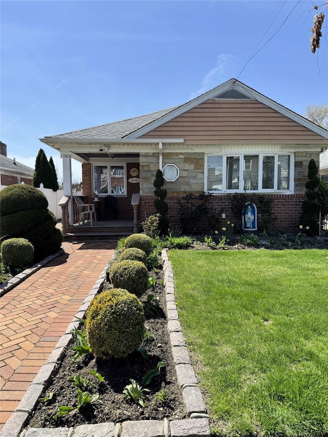 view of front of house featuring covered porch, a front lawn, and brick siding