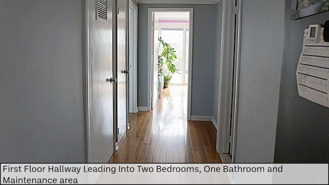 hall with baseboards, wood finished floors, and visible vents