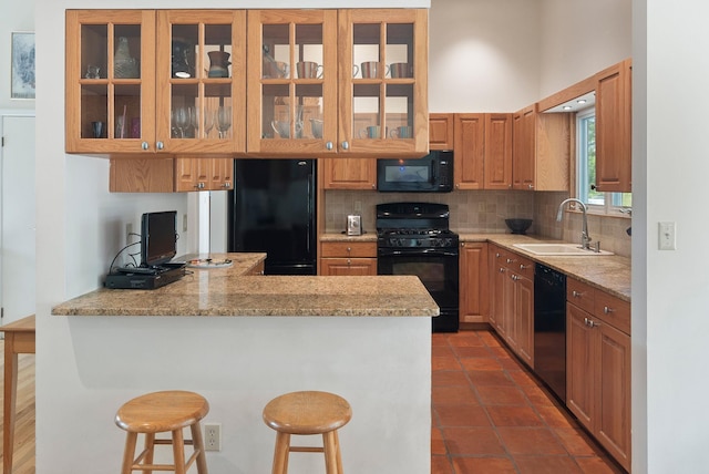 kitchen featuring glass insert cabinets, a sink, a peninsula, decorative backsplash, and black appliances