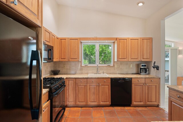 kitchen with a sink, light stone countertops, backsplash, and black appliances