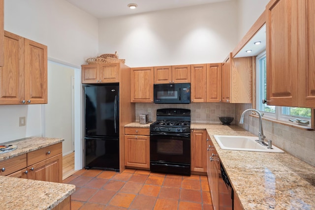 kitchen with a sink, light stone counters, black appliances, decorative backsplash, and a high ceiling