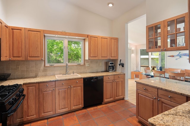 kitchen with plenty of natural light, light stone counters, a sink, black appliances, and tasteful backsplash